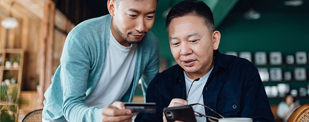 Medium Father And Son Looking Into Credit Card On Mobile Phone