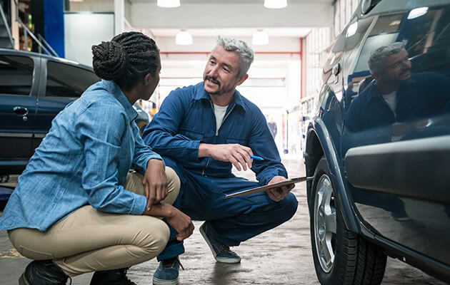 Large Mechanic Talking And Consulting With Customer In Car Garage