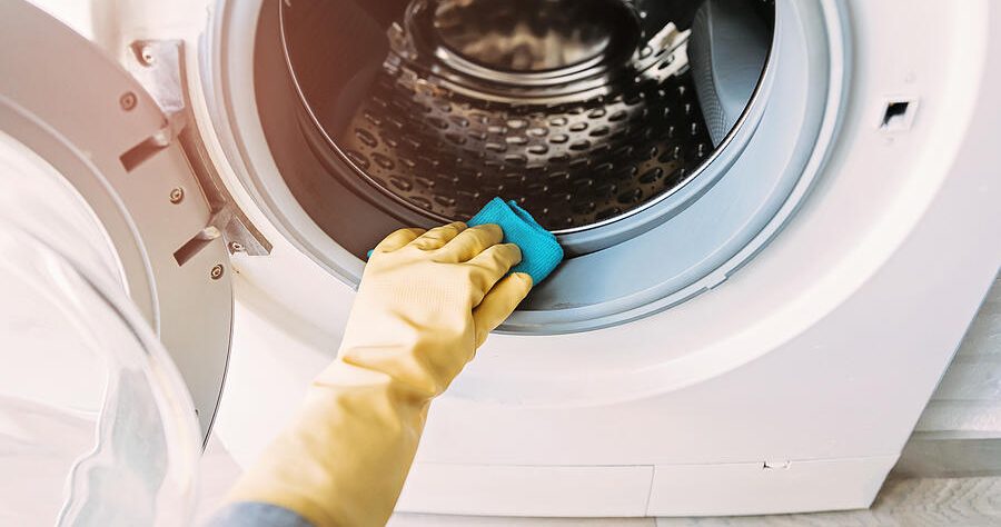 A hand in a glove cleans the inside of a front-loading washer.