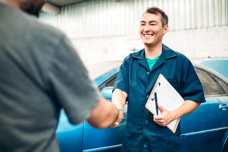 Auto body repair shop representative and customer shaking hands near the vehicle.