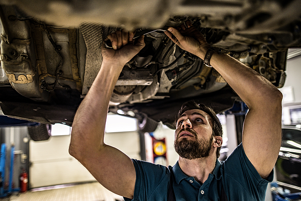 A mechanic repairing the underside of a car in an auto shop.