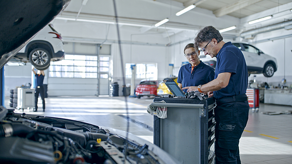 Two mechanics running tests on a vehicle in a repair shop.