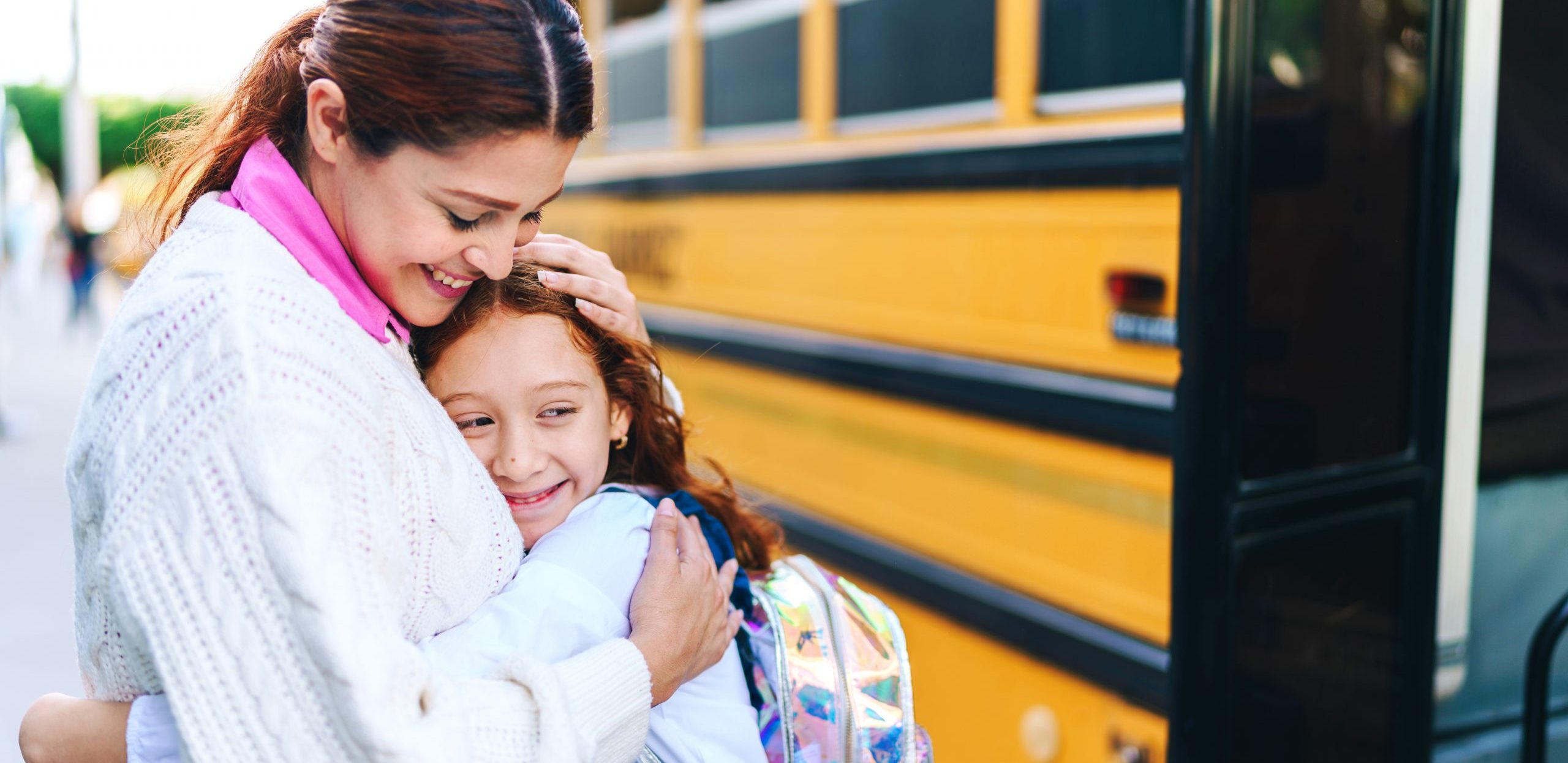 An elementary-aged girl embraces her mother before she gets on the school bus..