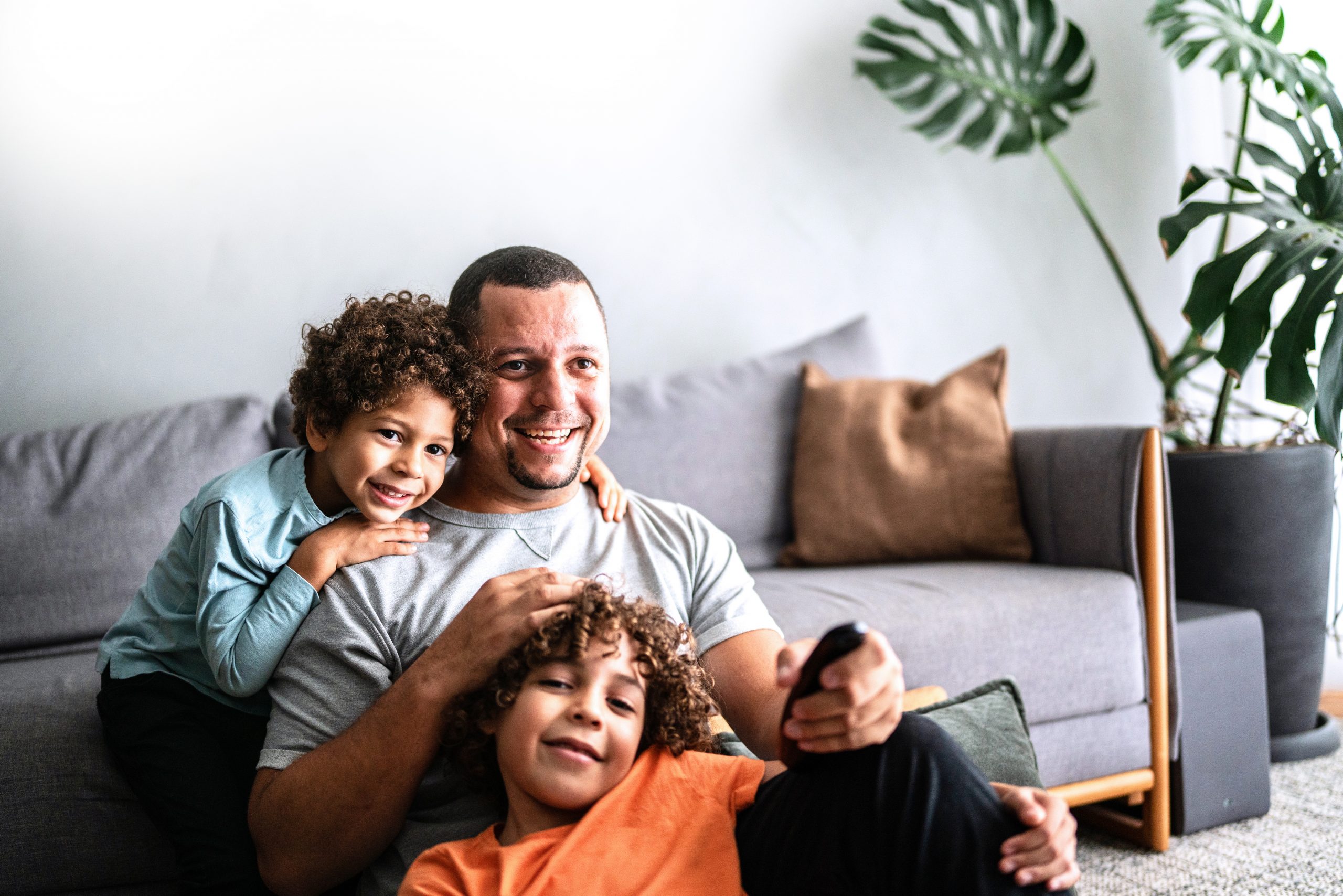 A dad and his young sons hang out together in the living room, watching a show.