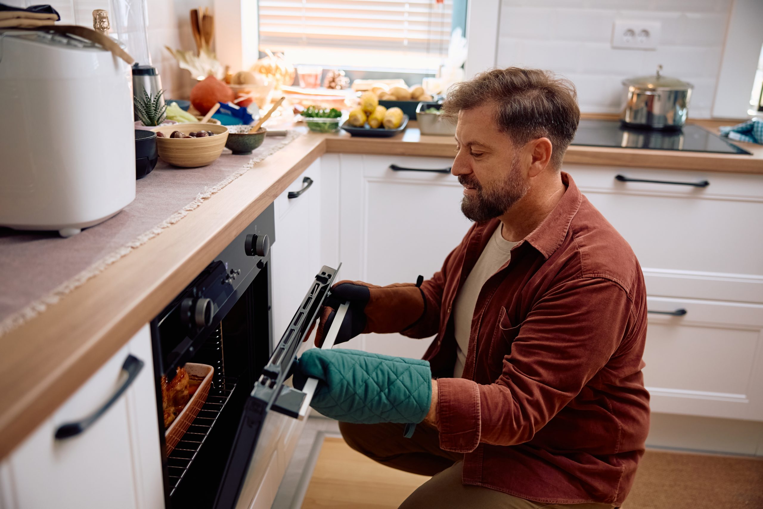 A middle-aged man peeks into his oven, checking on his roast.