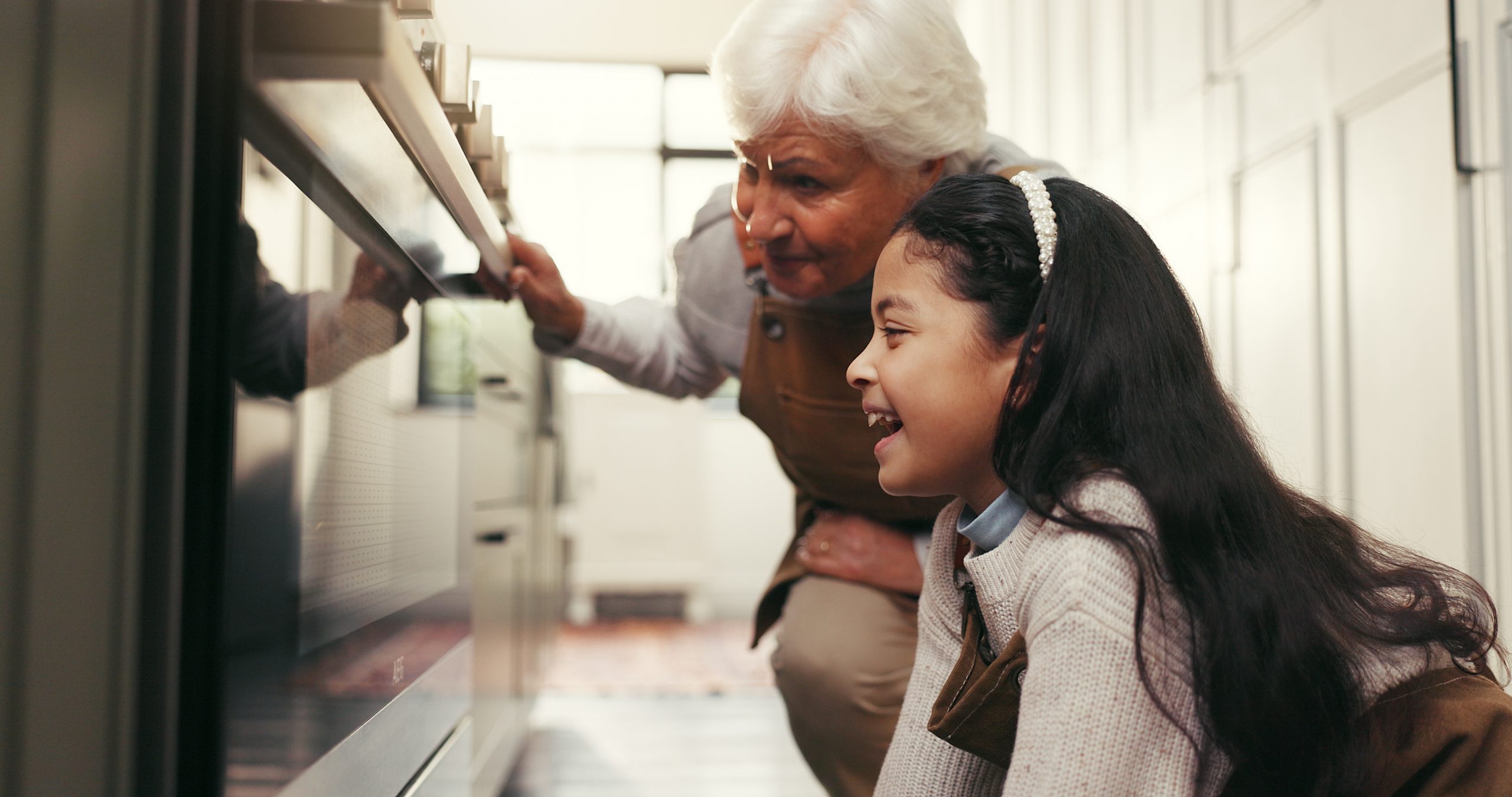A grandmother and her granddaughter check on cookies using the oven light.