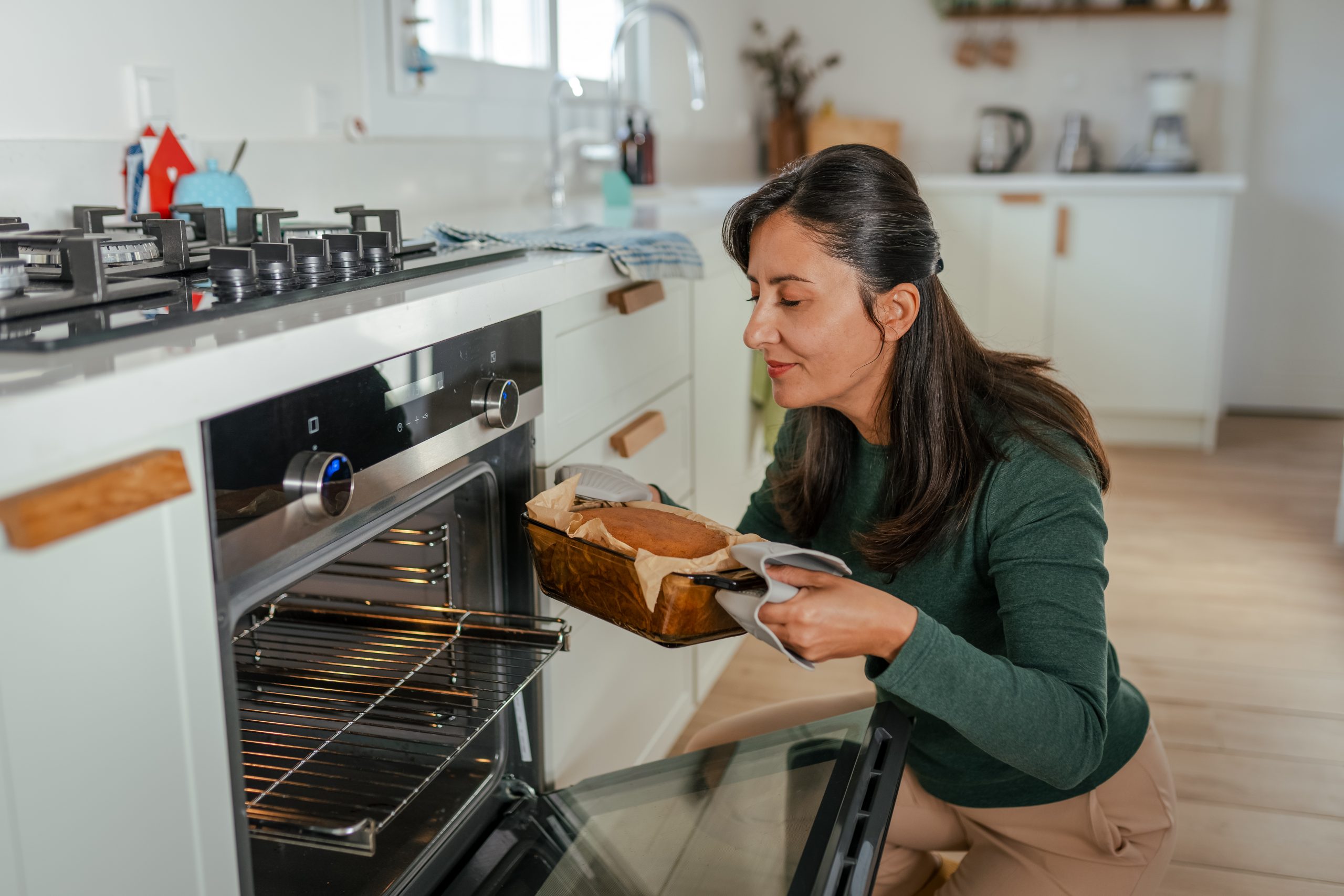 A woman takes out bread from her oven, enjoying the fresh smell of baked bread.
