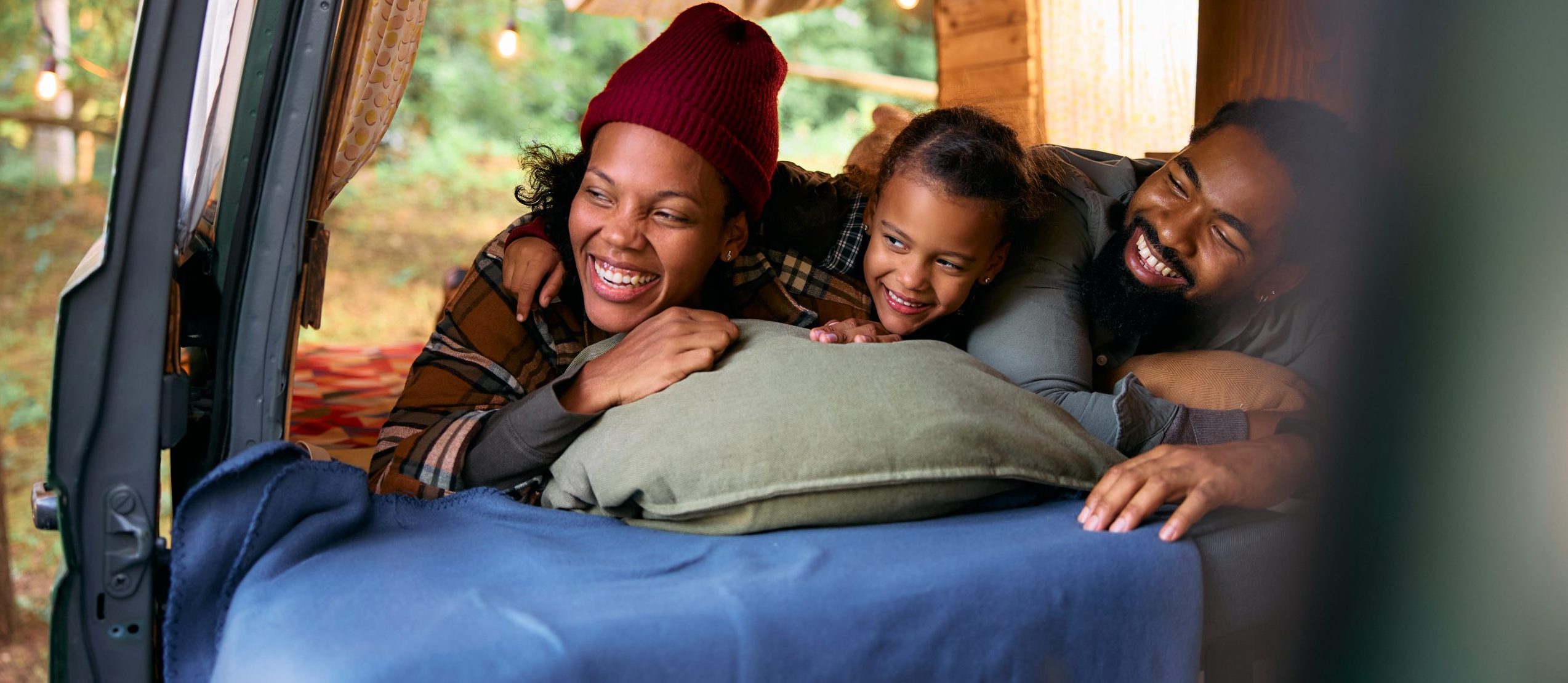 A family of three pile in the back of their vehicle, enjoying camping.