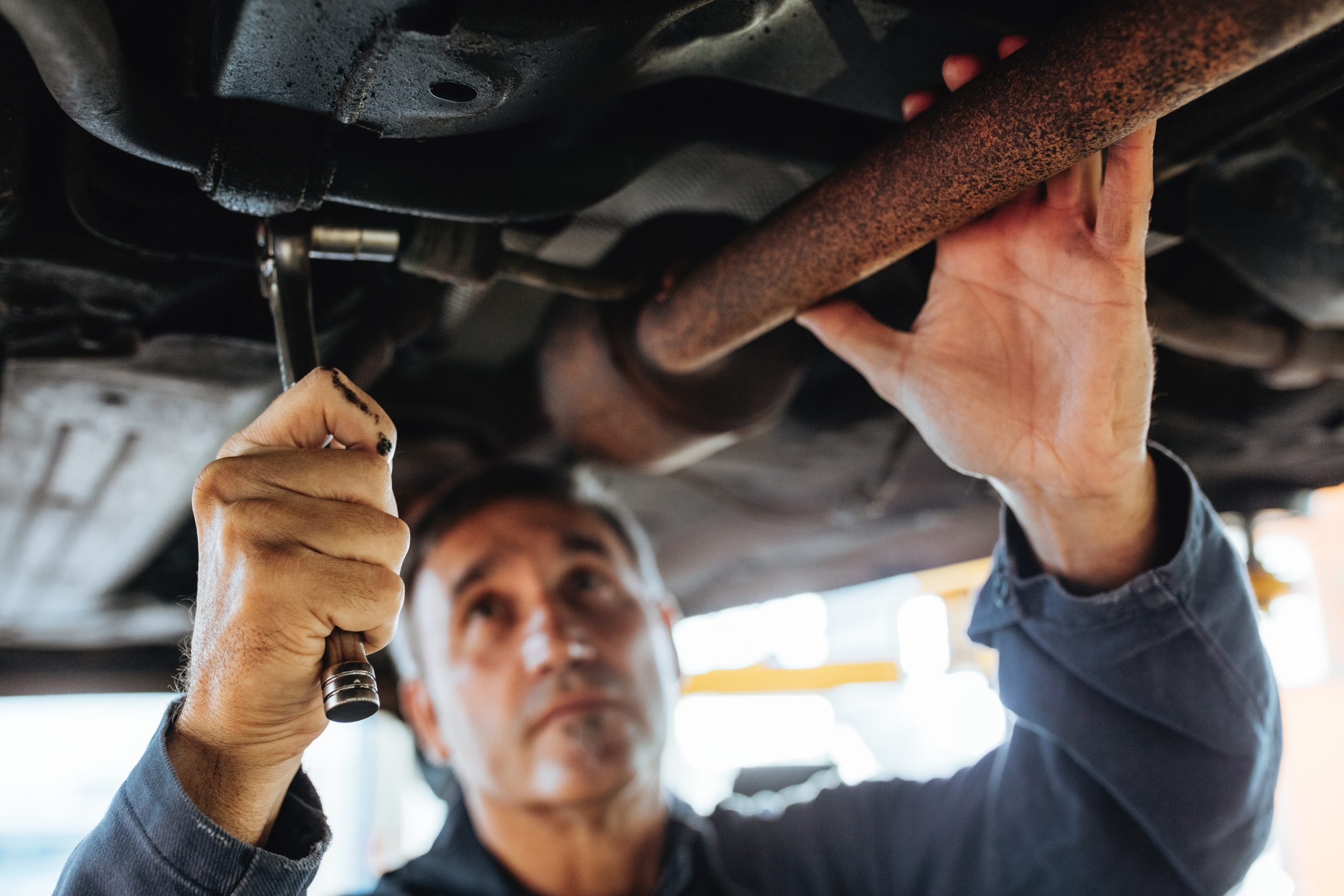 A man in blue works on repairing the underside of a car.