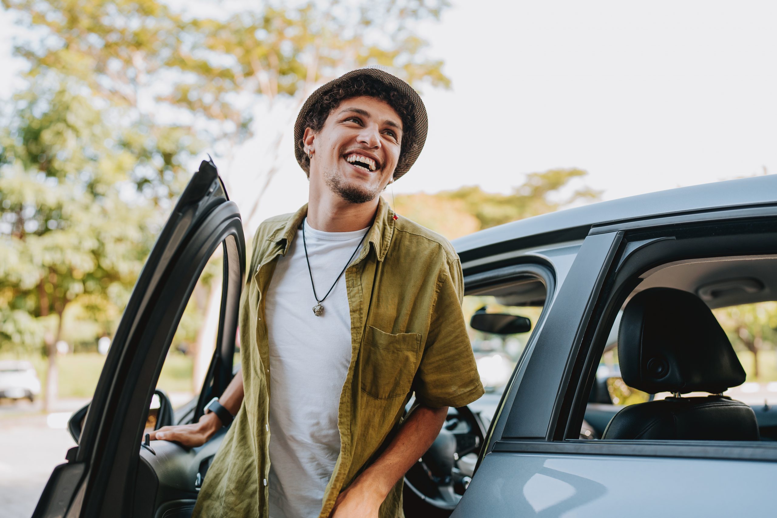 A smiling young man steps out of his car.