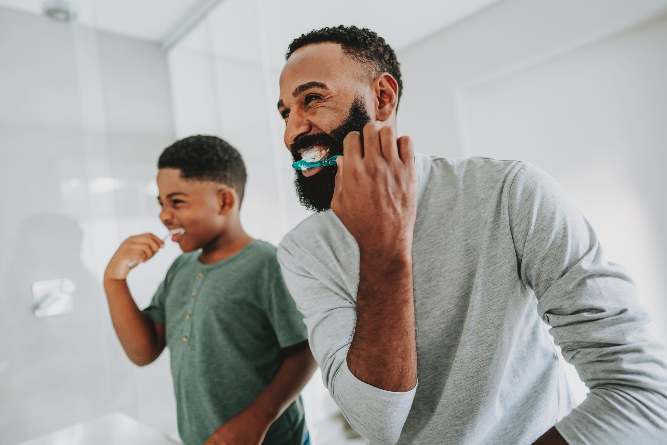 A father and son brush their teeth together in the bathroom.