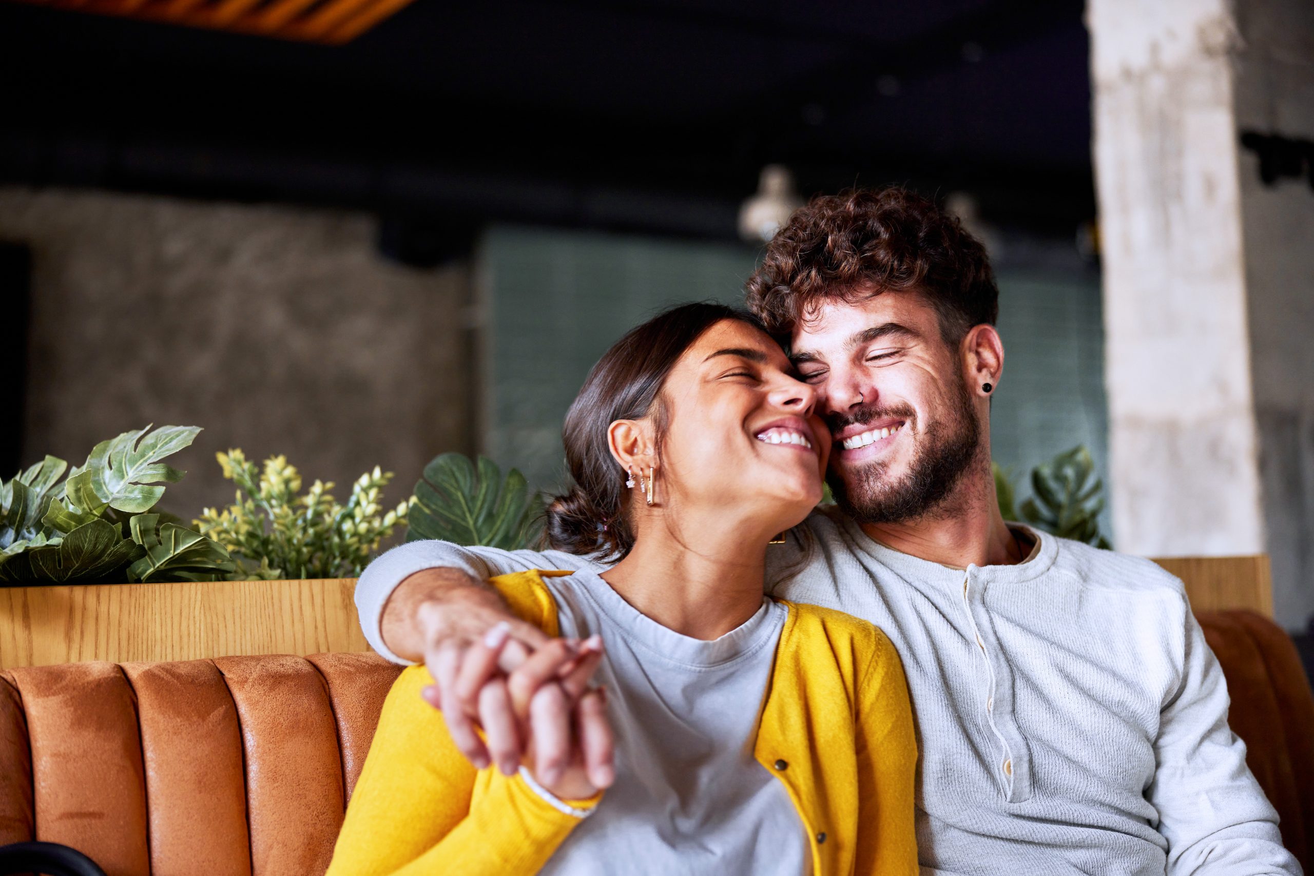 A young couple sits on a couch, happily smiling.