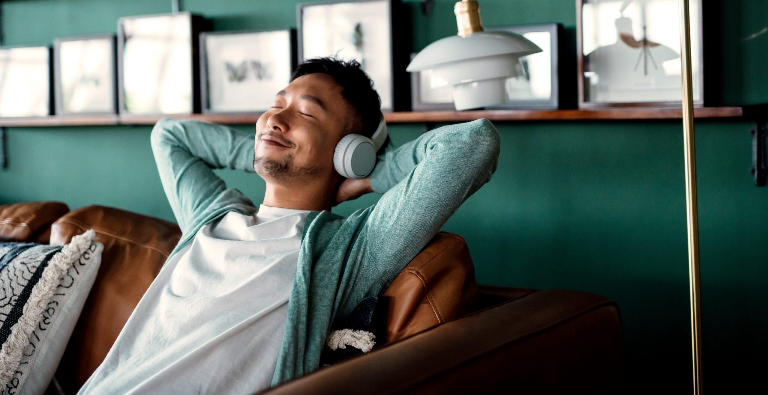 A man sits in a living room on a leather couch, with headphones on, enjoying music .