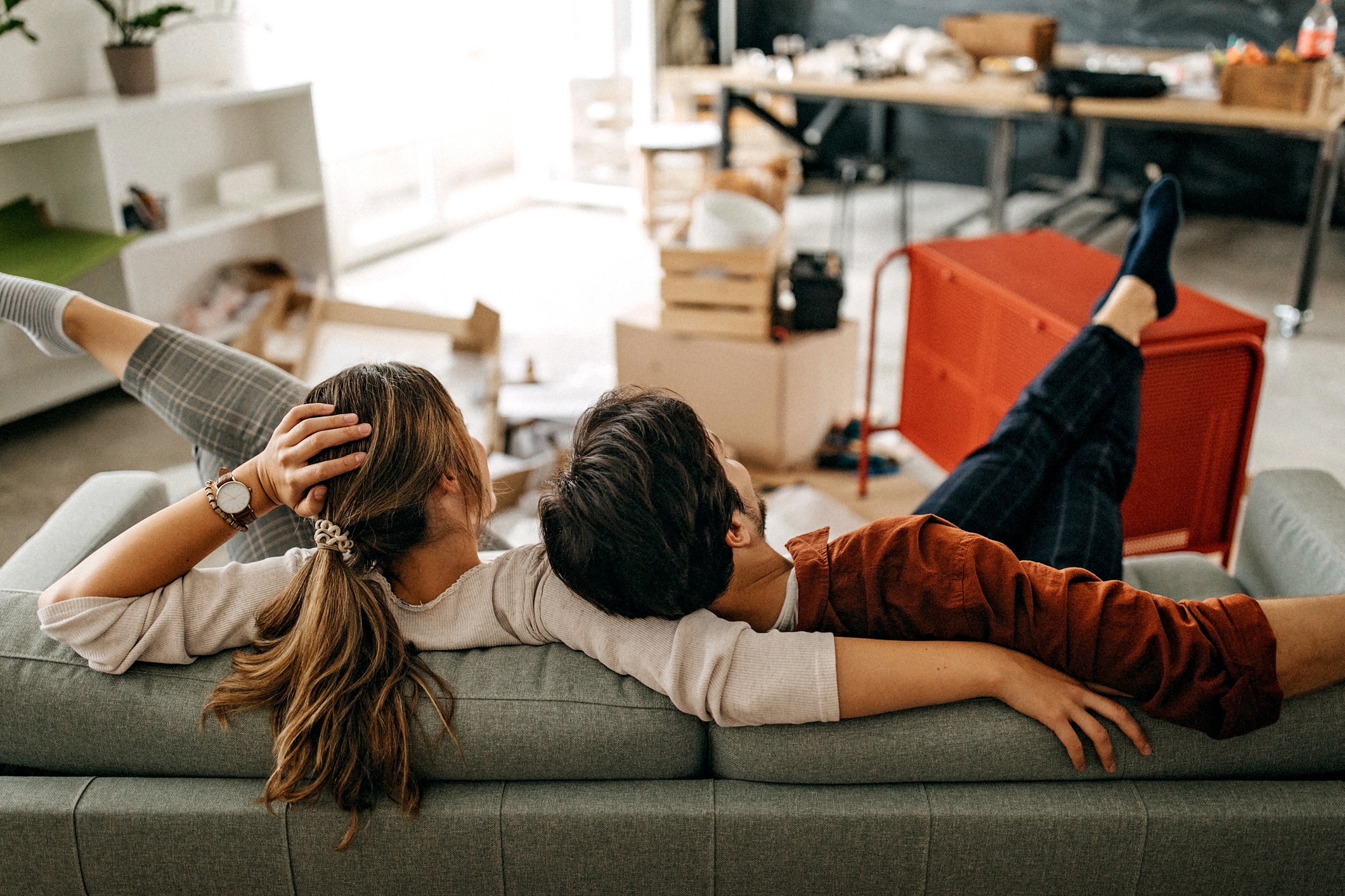 A couple relax on a sectional, facing their semi-unpacked room.
