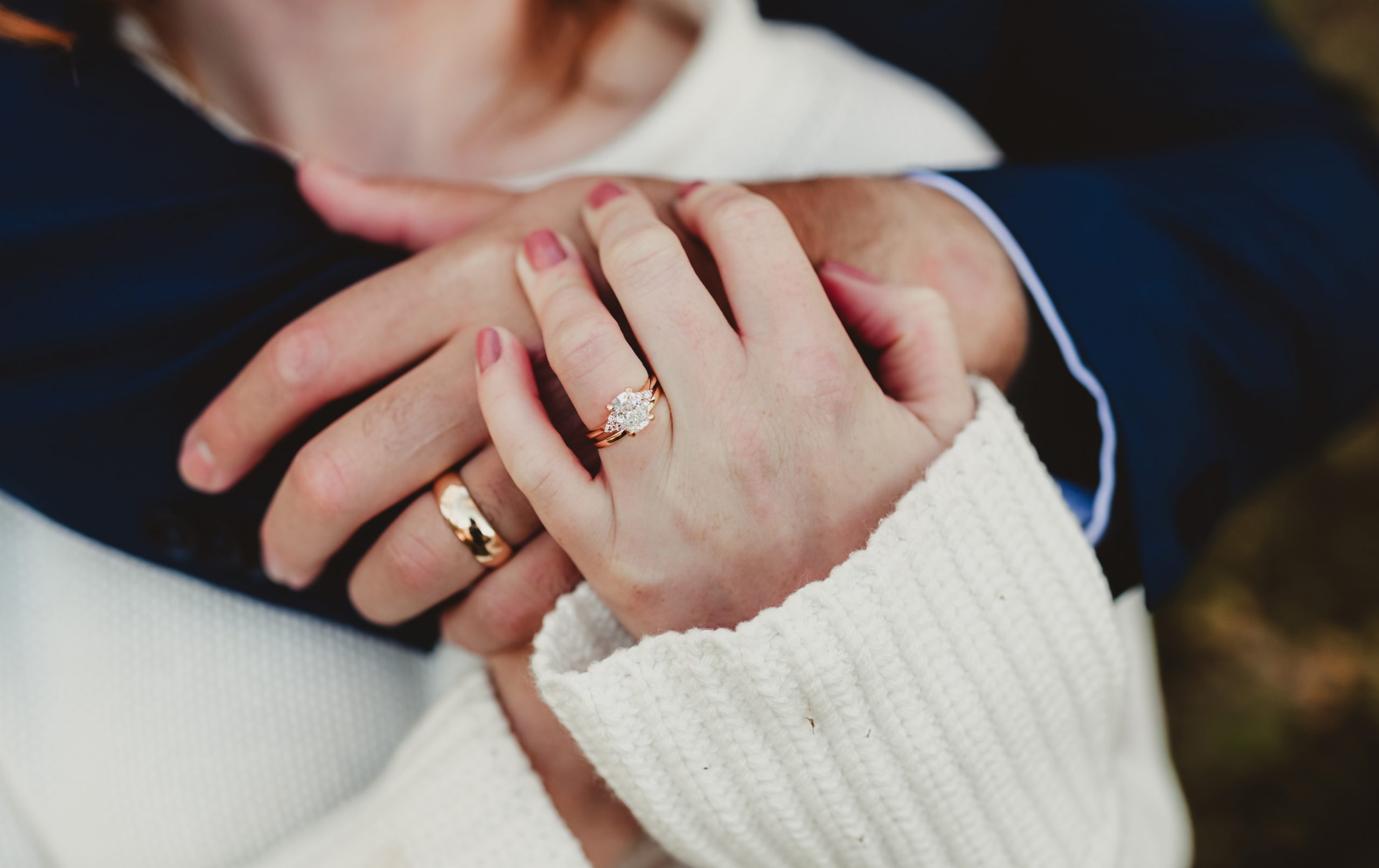 A man wraps his arms around a woman, both showcasing their engagement and wedding rings.