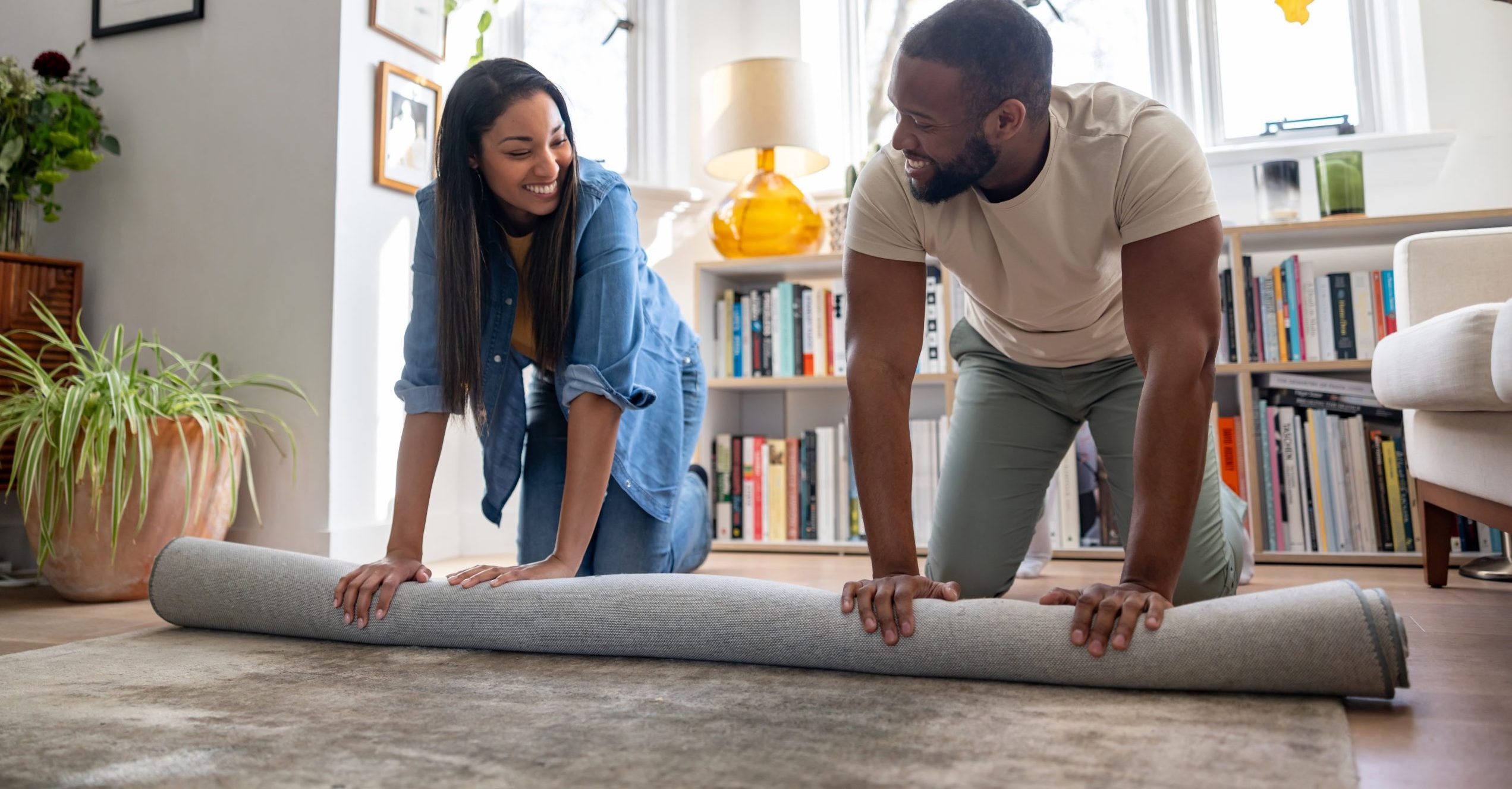 A couple unrolls a rug together in their first apartment.