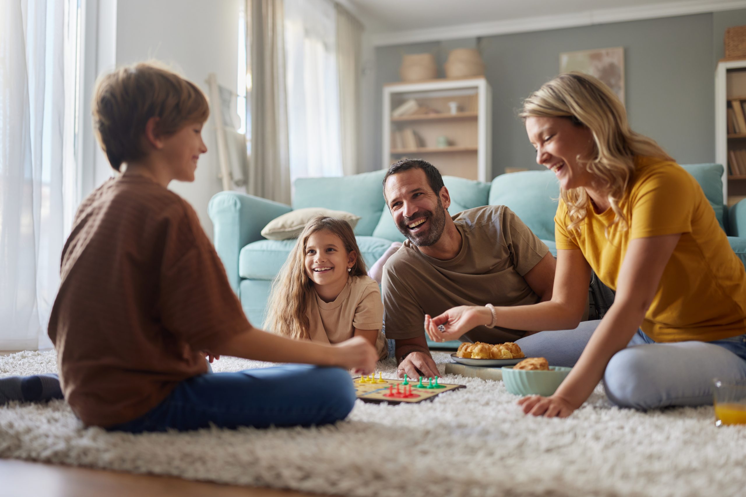 A family eats snacks and plays a board game in the living room.