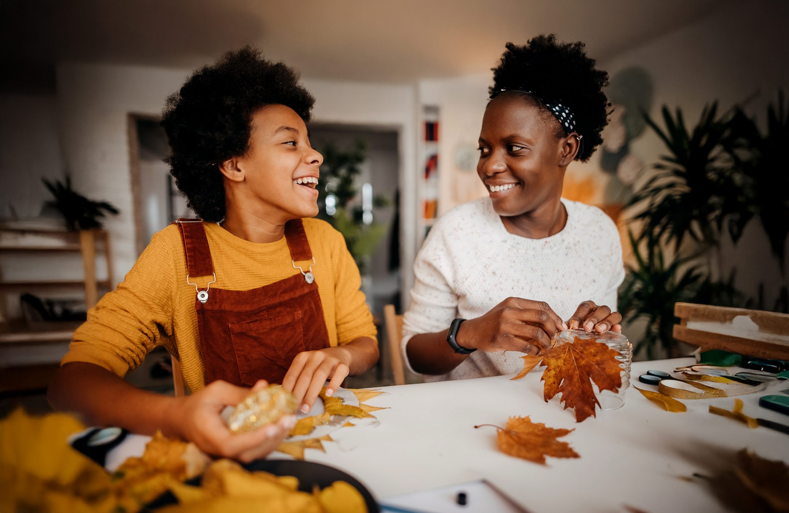 A mother and young son sit at a table making crafts with leaves