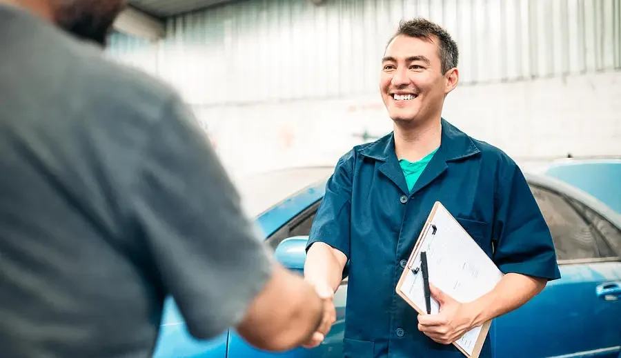 Auto body repair shop representative and customer shaking hands near the vehicle.
