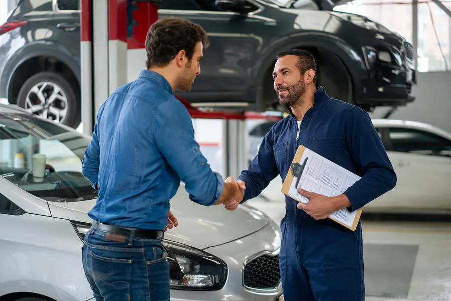 A customer and mechanic shaking hands near auto repairs.