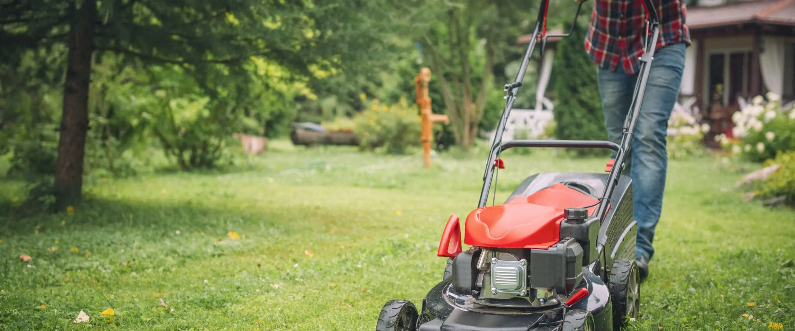 man pushing lawn mower across yard hero